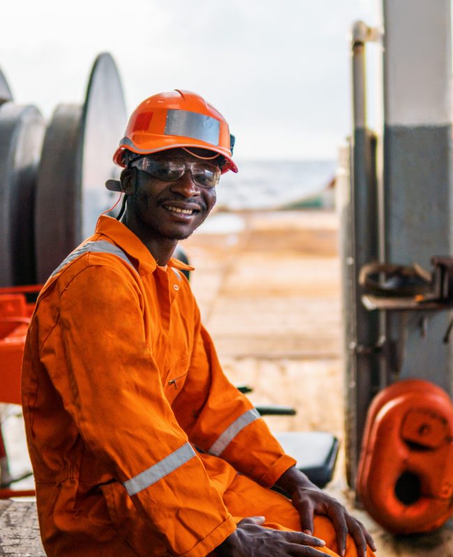 happy Seaman AB or Bosun on deck of vessel or ship , wearing PPE personal protective equipment - helmet, coverall, lifejacket, goggles. Safety at sea